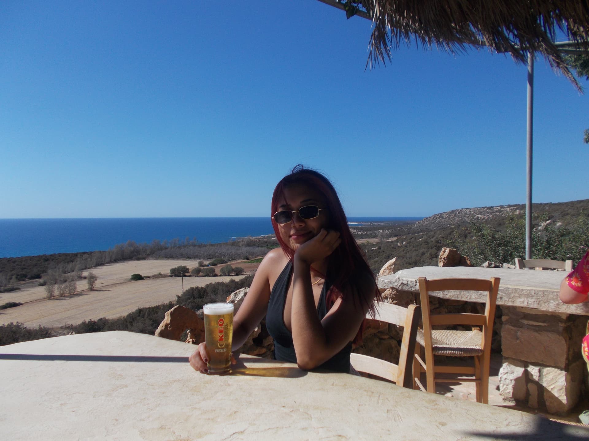 Image of Lyla holding a Keo beer with a pictureque of the sea in the background